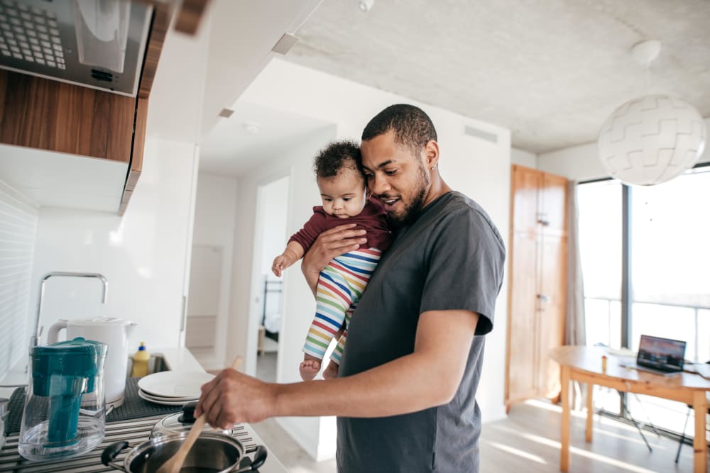 Father cooking in his new kitchen with his child under one arm at Ascend in Portland, Oregon