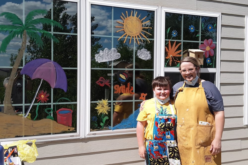 Artist and a young child standing in front of painted windows outside Keelson Harbour in Spirit Lake, Iowa