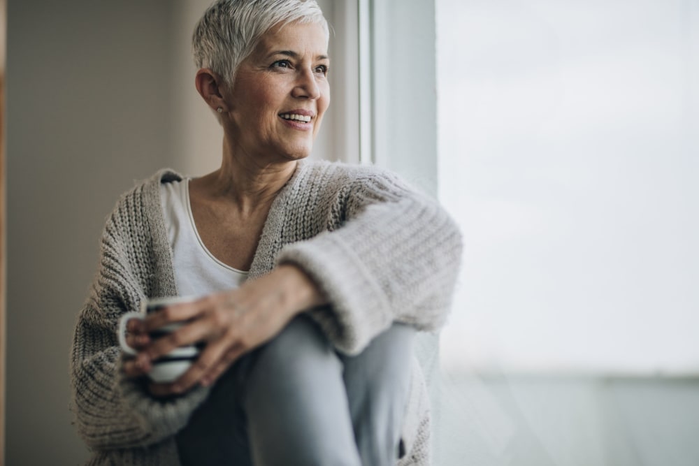 Resident looking out the window and drinking coffee at Campus Commons Senior Living in Sacramento, California