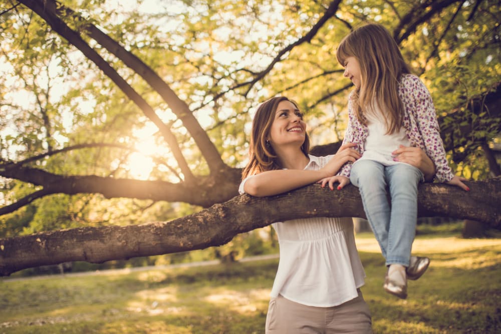 Mother with daughter as she enjoys herself climbing a tree near The Park at Ashford in Arlington, Texas