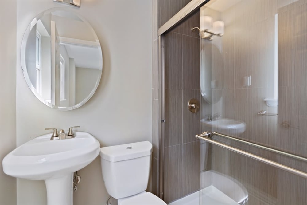 Cute circle vanity mirror and sliding glass shower food in the bathroom at Eagle Rock Apartments at North Plainfield in North Plainfield, New Jersey