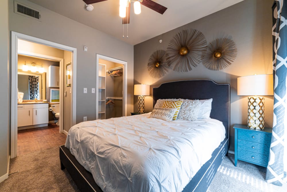 Carpeted bedroom with full size bed and modern style furniture, walk-in closet, and private bathroom at Marquis at Texas Street in Dallas, Texas