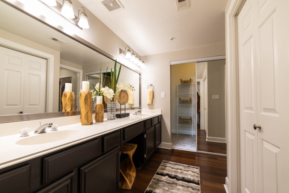 Large bathroom with double sinks, wood flooring, and separate walk-in closet at Marquis at Great Hills in Austin, Texas