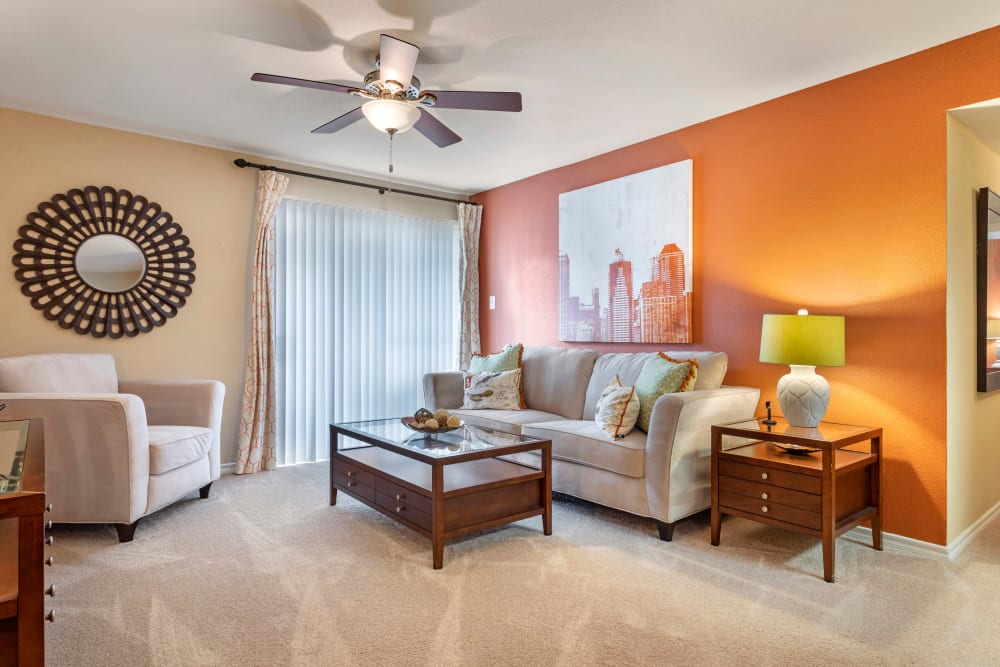 Comfortable living room with plush carpeting and a ceiling fan in a model apartment home at Foundations at Austin Colony in Sugar Land, Texas