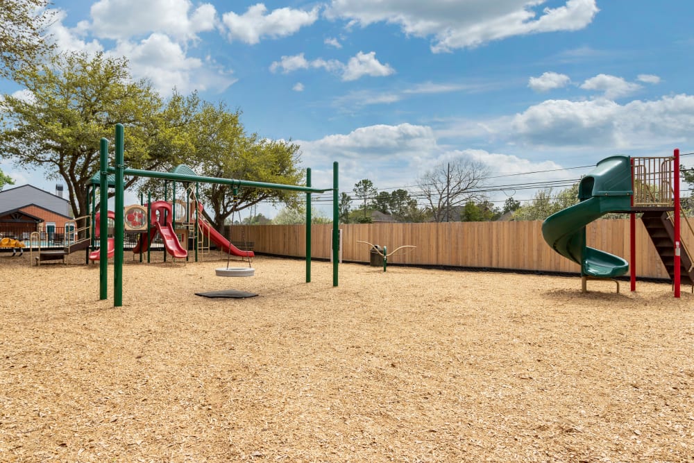 Large sunny play area for children with play structures and a tire swing at Foundations at Austin Colony in Sugar Land, Texas