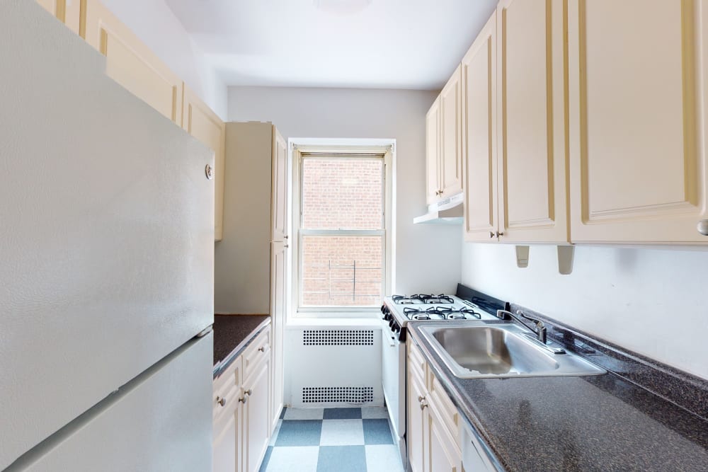 Checked floors with black countertops and light wood cabinets in the kitchen at Eastgold NYC in New York, New York