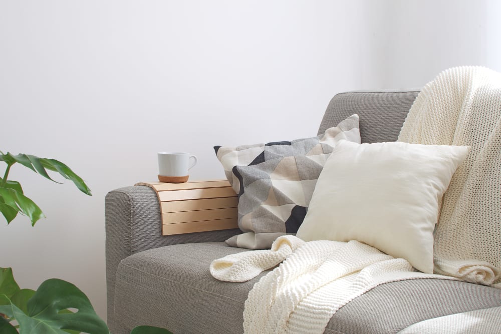 Couch with an arm caddy and a cup of tea on it in a model home at K Street Flats Apartment Homes in Berkeley, California