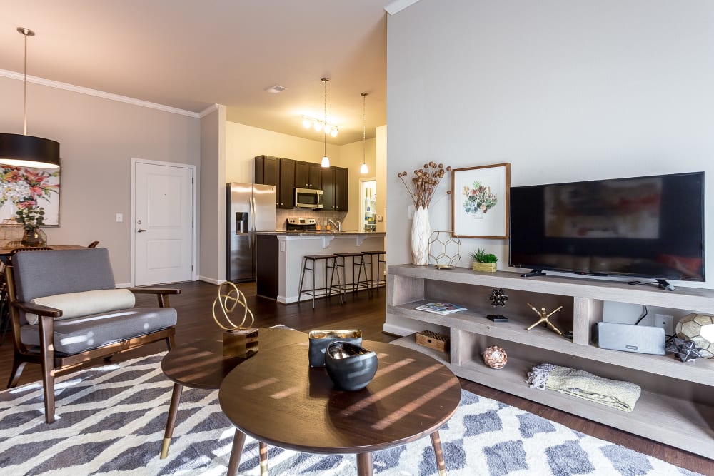 Living room with wood-style flooring and modern kitchen with counter seating in a model home at Creekside at Greenlawn Apartment Homes in Columbia, South Carolina