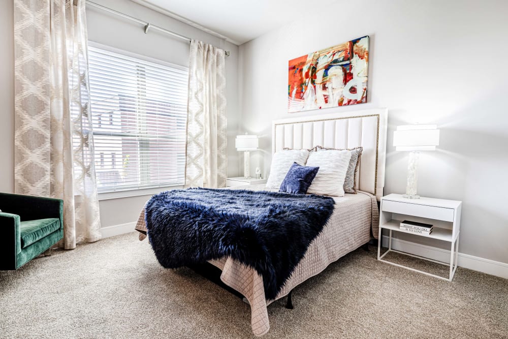 Apartments in Clayton, MO for Rent - The Barton - Bedroom with a Bed, Two Nightstands, a Chair, Carpet Flooring, and a Window