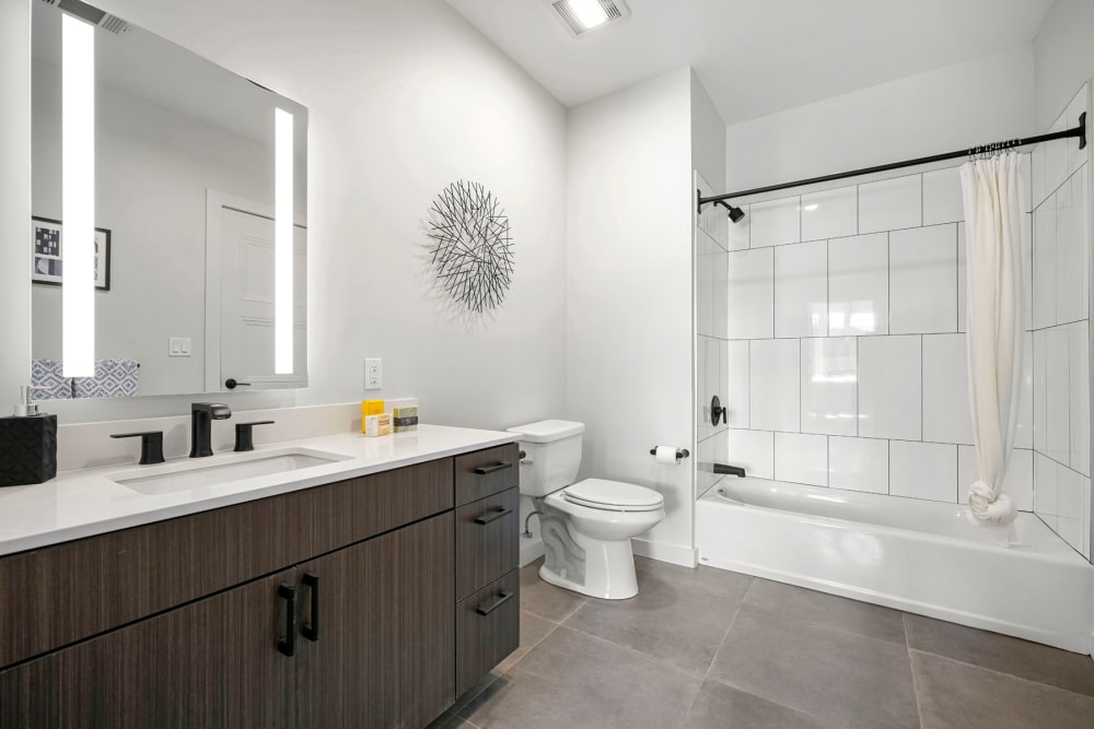 Custom tiled shower and a large vanity mirror in a model apartment's bathroom at Anden in Weymouth, Massachusetts