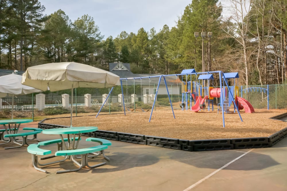 Large playground with tables and umbrellas next to it so you can relax while the kids play at Arbor Crossing Apartments in Lithonia, Georgia