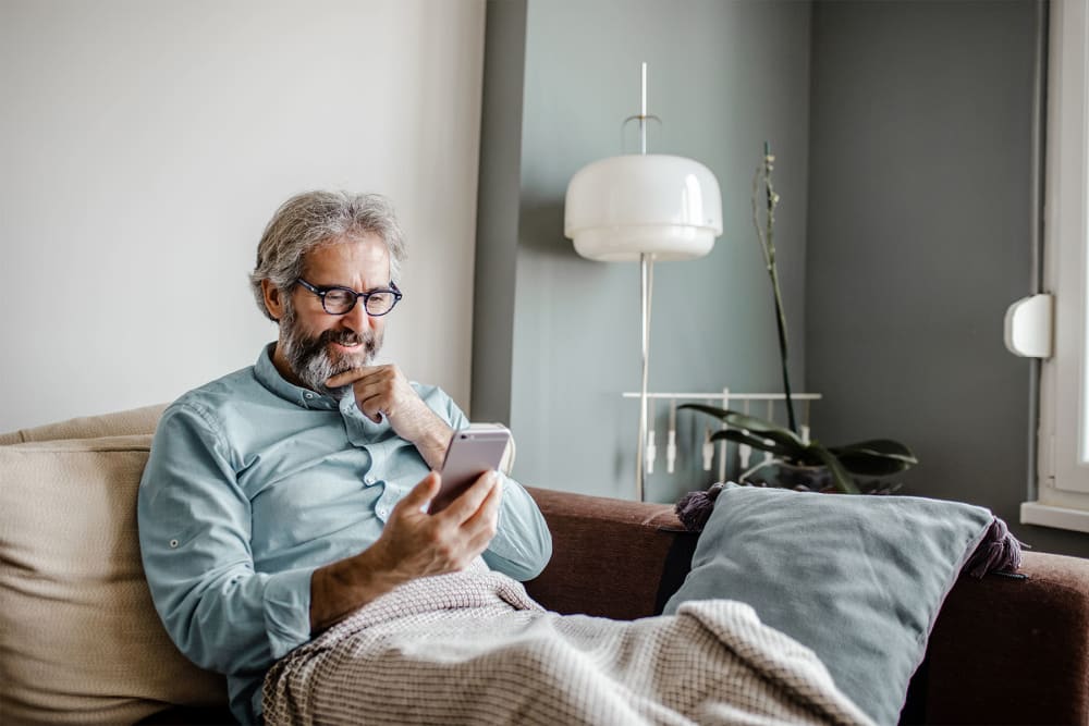 Resident surfing the web on a mobile phone from the comfort of the couch in his new home at parcHAUS AT CELINA PARKWAY in Celina, Texas