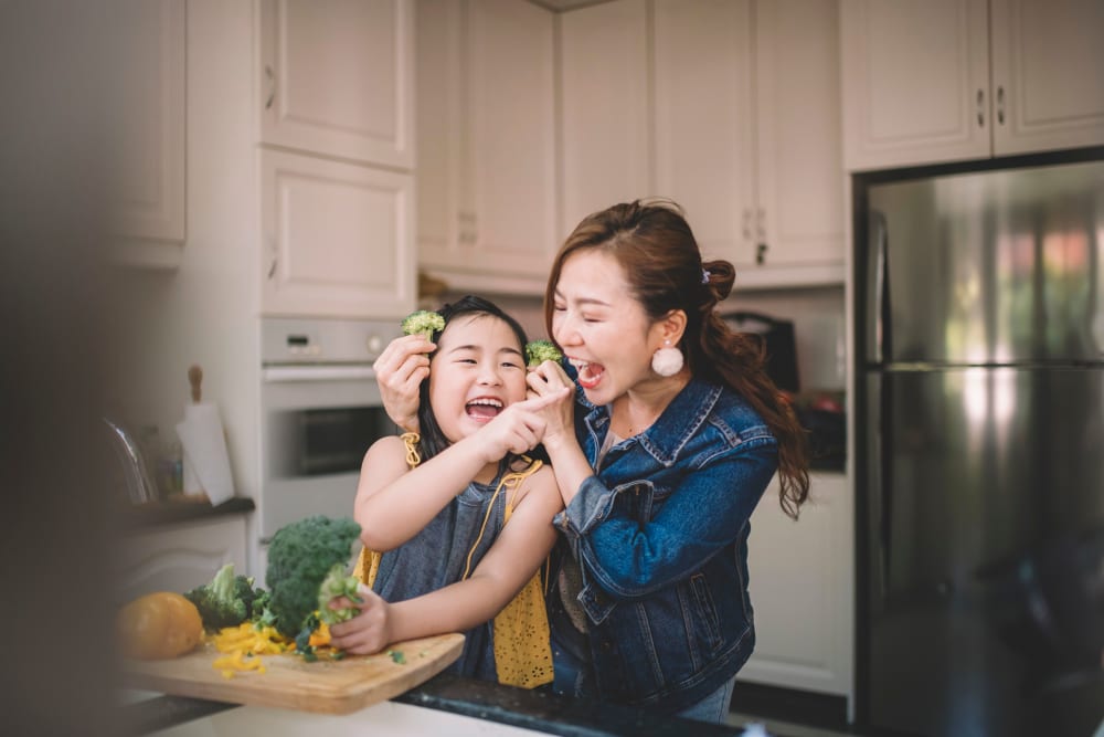Mother and daughter having some fun while cutting up fresh vegetables in their modern kitchen at parcHAUS AT CELINA PARKWAY in Celina, Texas