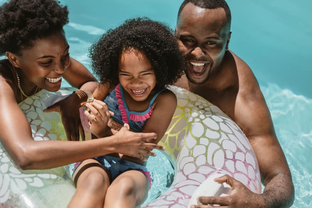 Family playing with their child in the pool on an inner tube at Woods of Williamsburg Apartments in Williamsburg, Virginia