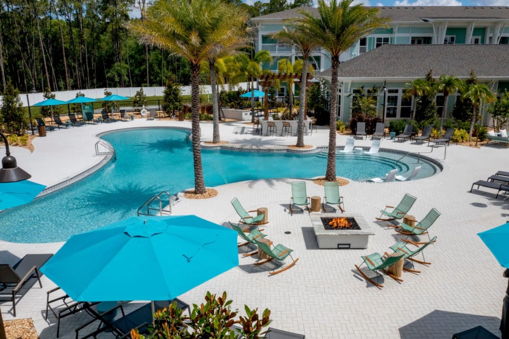 Lutz, FL Apartments - Sage at Cypress - Pool Area with White and Black Lounge Chairs, Tables, Surrounded by Palm Trees and Fire Pit Area