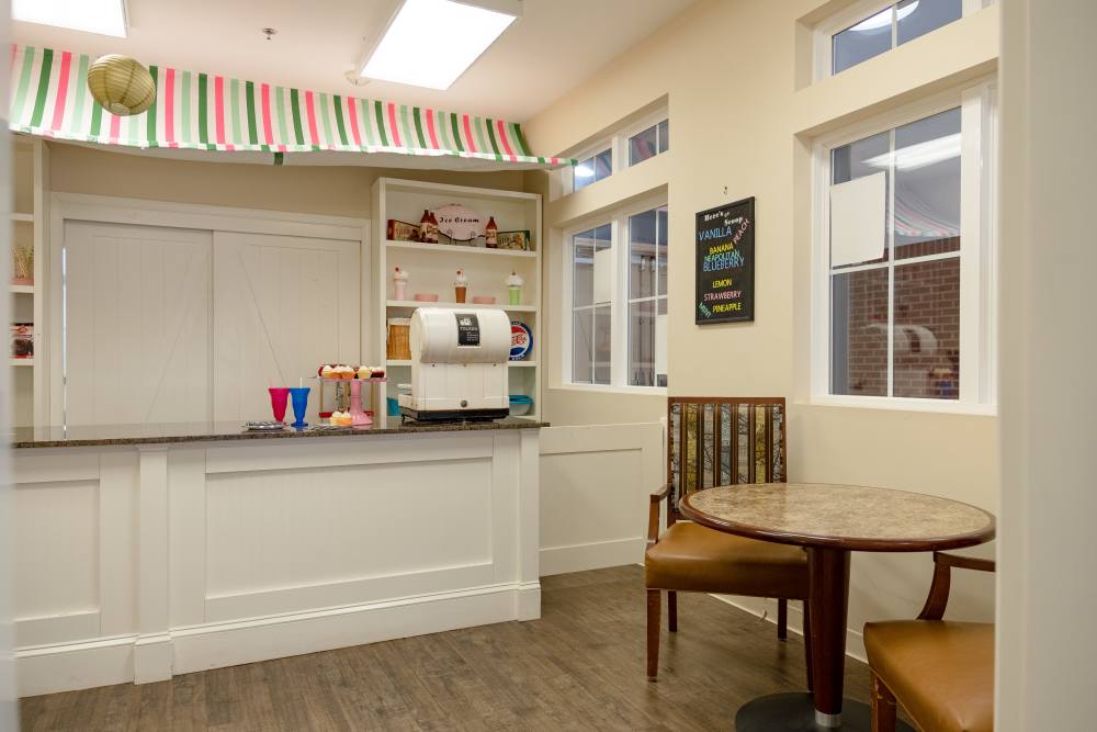  A bright and welcoming apartment kitchen with white cabinets, dining table and a coffee bar at The Harmony Collection at Roanoke - Memory Care in Roanoke, Virginia