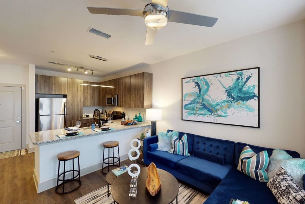 Apartment living room with blue couch, wall art, and ceiling fan at Soba Apartments in Jacksonville, Florida