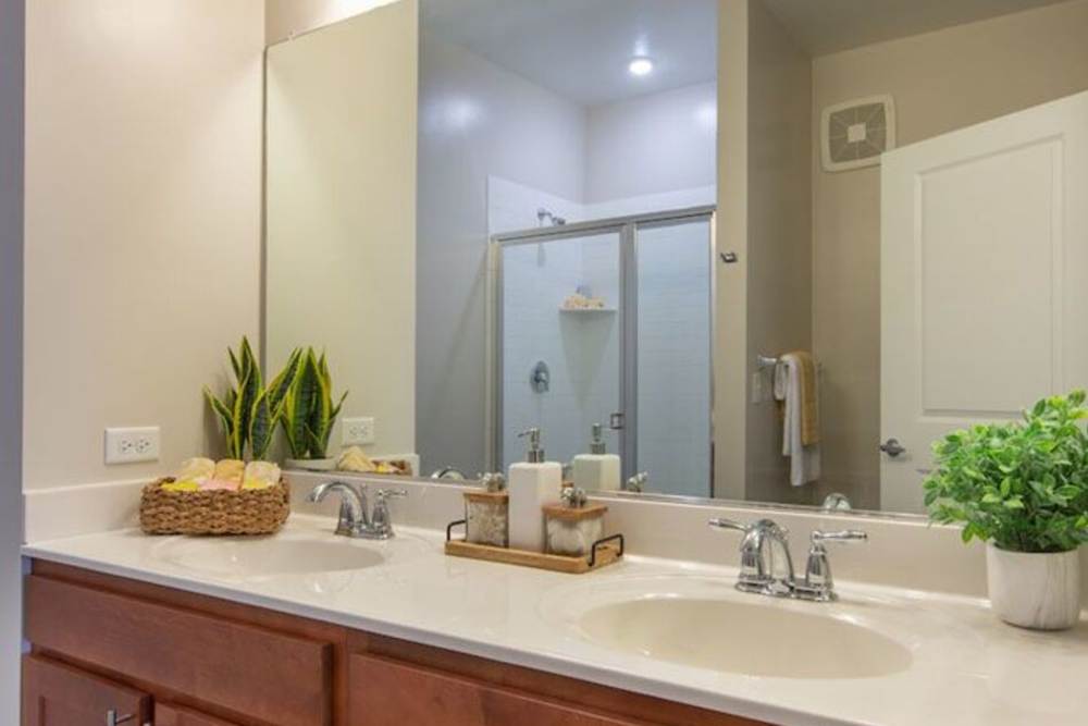 Modern, well lit bathroom with sink, big mirror and wooden storage space at The Elms at Century in Germantown, Maryland