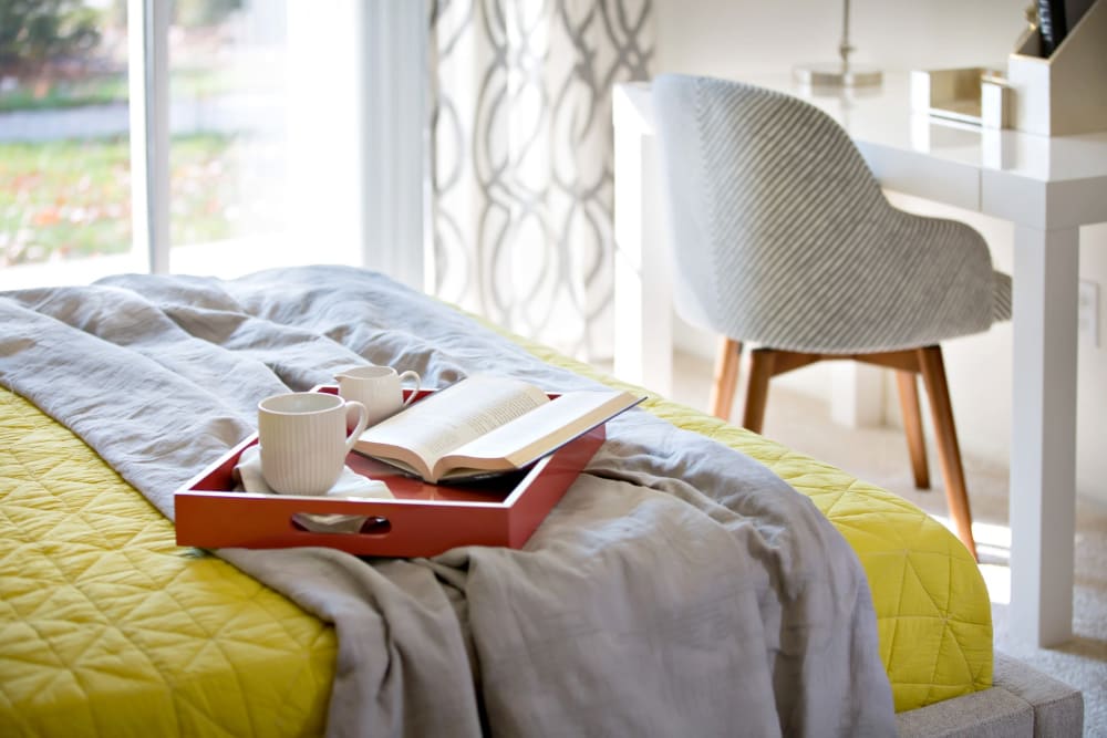 Tray with hot beverages and book on top of resident bed at Artisan at Lawrenceville in Lawrenceville, New Jersey