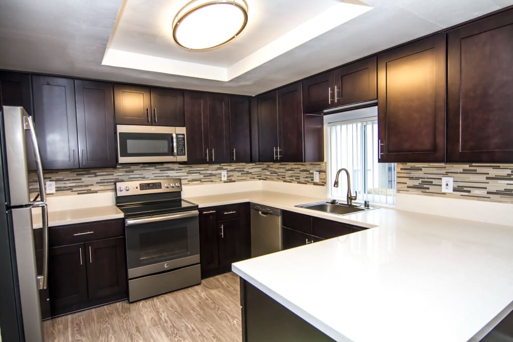Apartment kitchen with white countertops and dark wood cabinets at Canyon Crest Views Apartments in Riverside, California