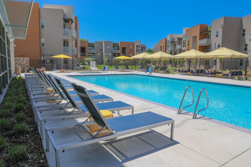 Sparkling pool with lounge chairs and umbrella at Sutter Green Apartments, Sacramento, California