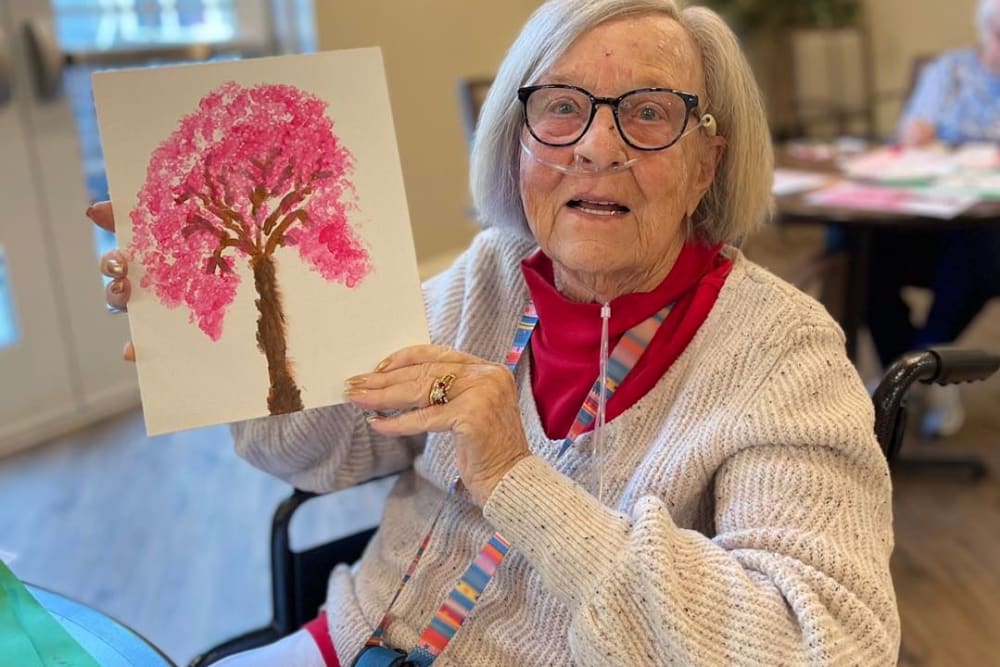 Resident holding a painted picture of tree at Harmony Senior Services