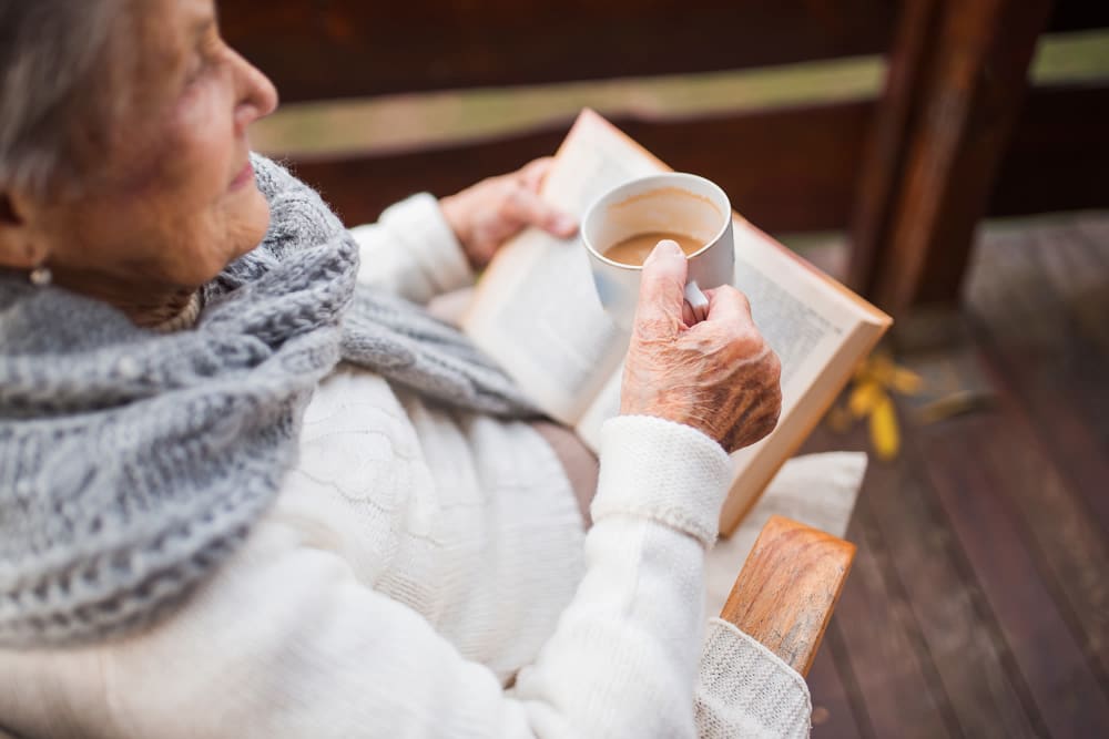 Elderly woman reading a book and drinking coffee at Vista Prairie at Goldfinch Estates