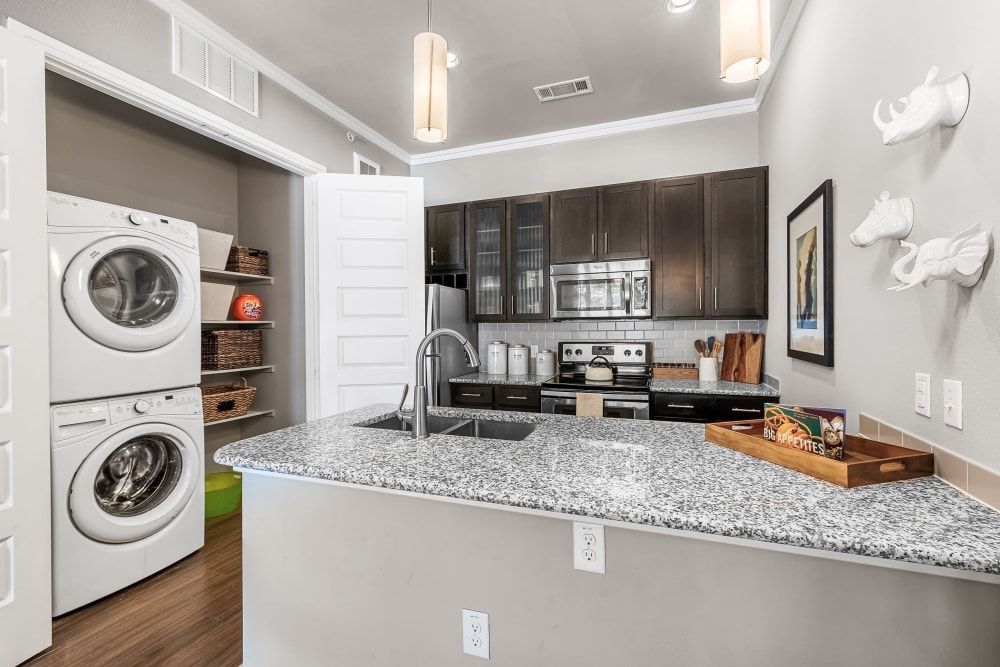 Beautiful kitchen with Custom Espresso Cabinetry, Stainless-Steel Appliances, and Granite Countertops and full size washer/dryer set at Marquis at Barton Trails in Austin, Texas