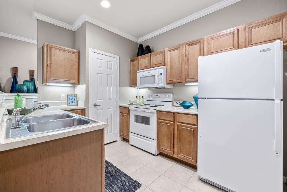 Bright kitchen with white appliances and wood cabinets and separate closed pantry at Marquis at The Cascades in Tyler, Texas
