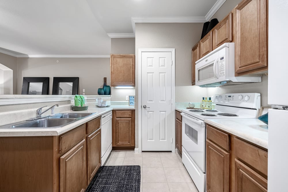Bright kitchen with white appliances and wood cabinets facing dining area at Marquis at The Cascades in Tyler, Texas