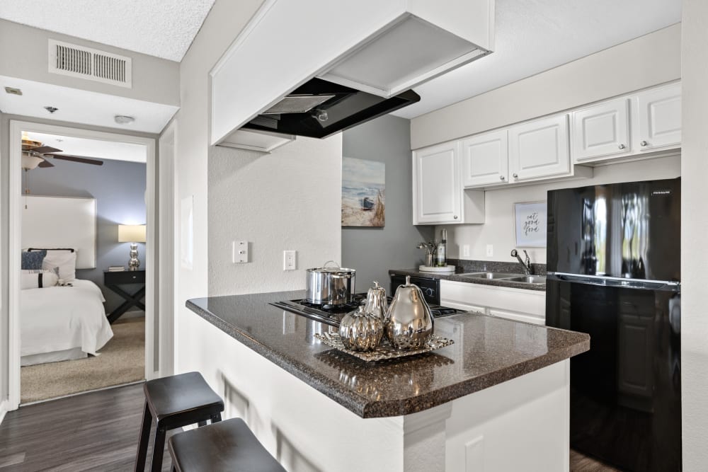Apartment kitchen with granite counters and black fridge at The Hills of Corona in Corona, California