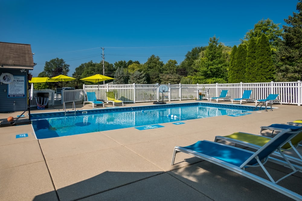 Community pool at Waters Edge Apartments in Lansing, Michigan, features lounge, chairs, and shade umbrellas