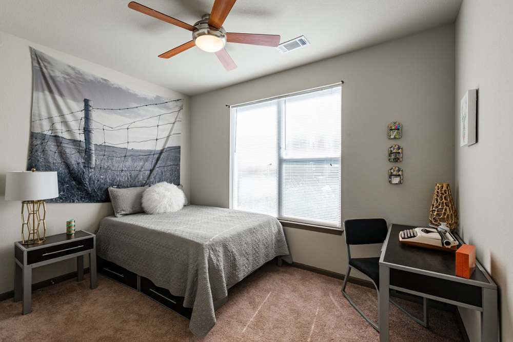 Carpeted bedroom with sunlit window and ceiling fan at The Quarters at Stillwater in Stillwater, Oklahoma