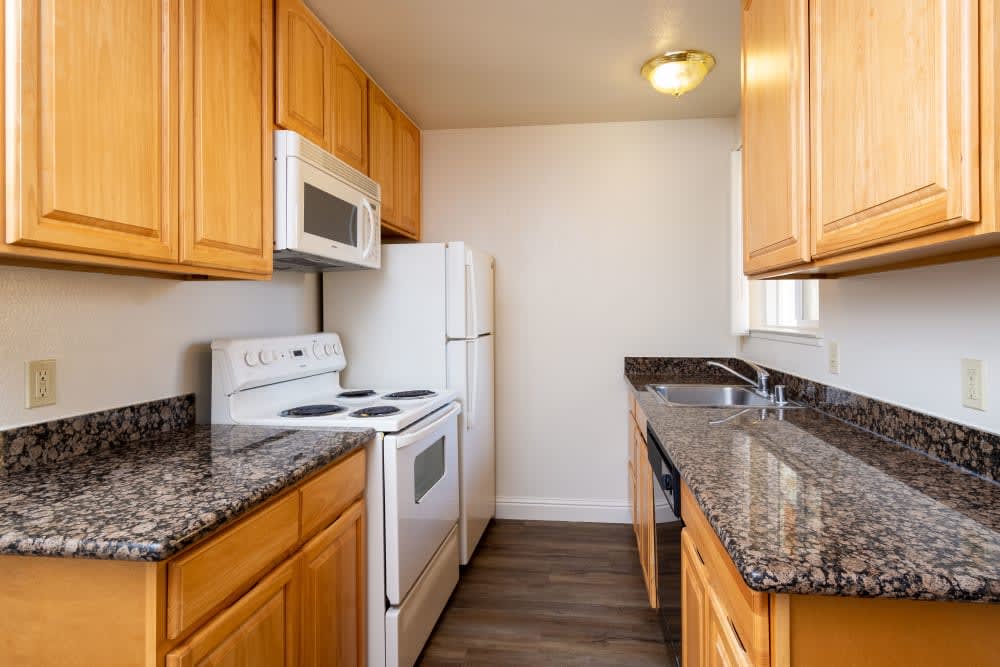 Fully equipped kitchen with dark countertops and white appliances at Peppertree Apartments in San Jose, California