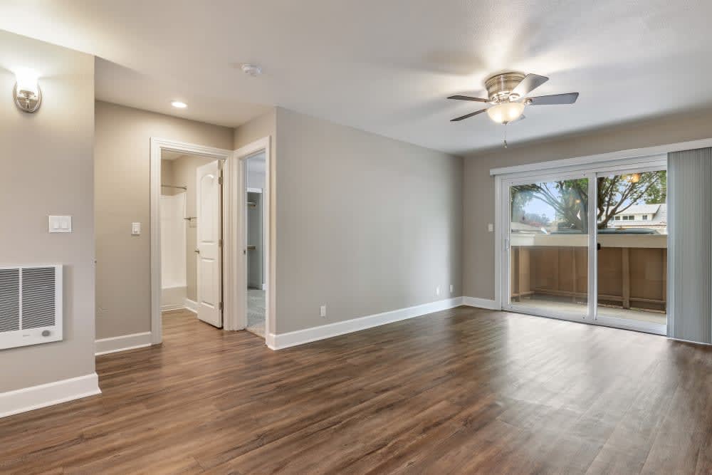 Living room with wood-style flooring and a ceiling fan opening onto a private patio at Pentagon Apartments in Fremont, California