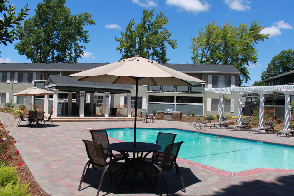 Outdoor swimming pool and sundeck patio table with an umbrella at Pinebrook Apartments in Fremont, California