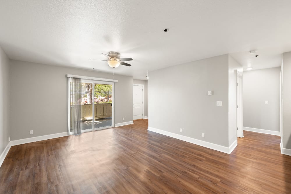 Spacious living room with wood-style flooring and sliding doors onto a private balcony at Summerhill Terrace Apartments in San Leandro, California