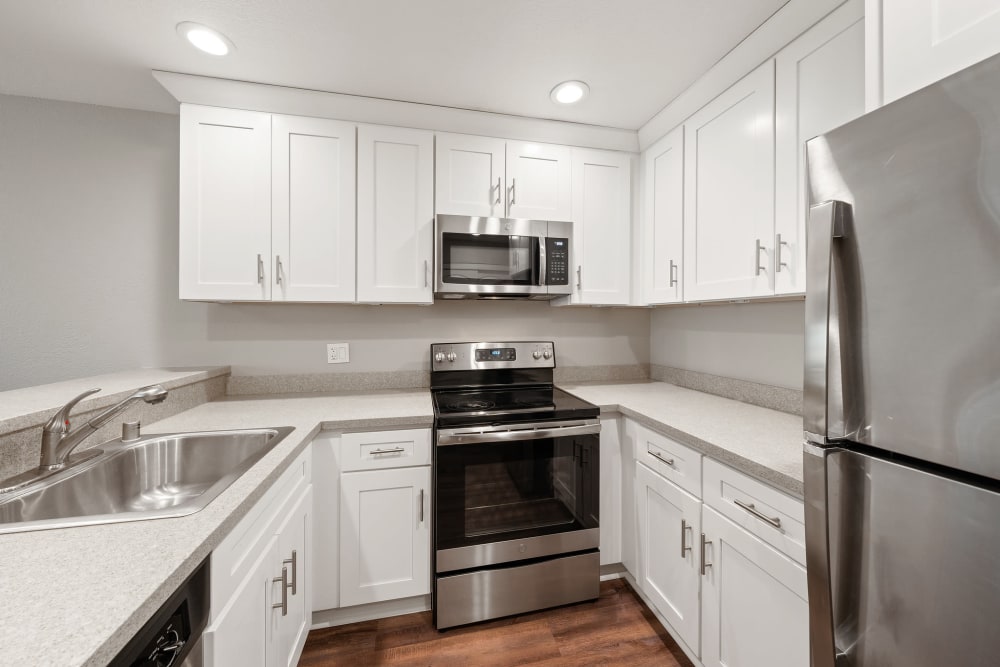 Fully equipped kitchen with white cabinetry, stainless-steel appliances, and a stainless-steel sink at Summerhill Terrace Apartments in San Leandro, California