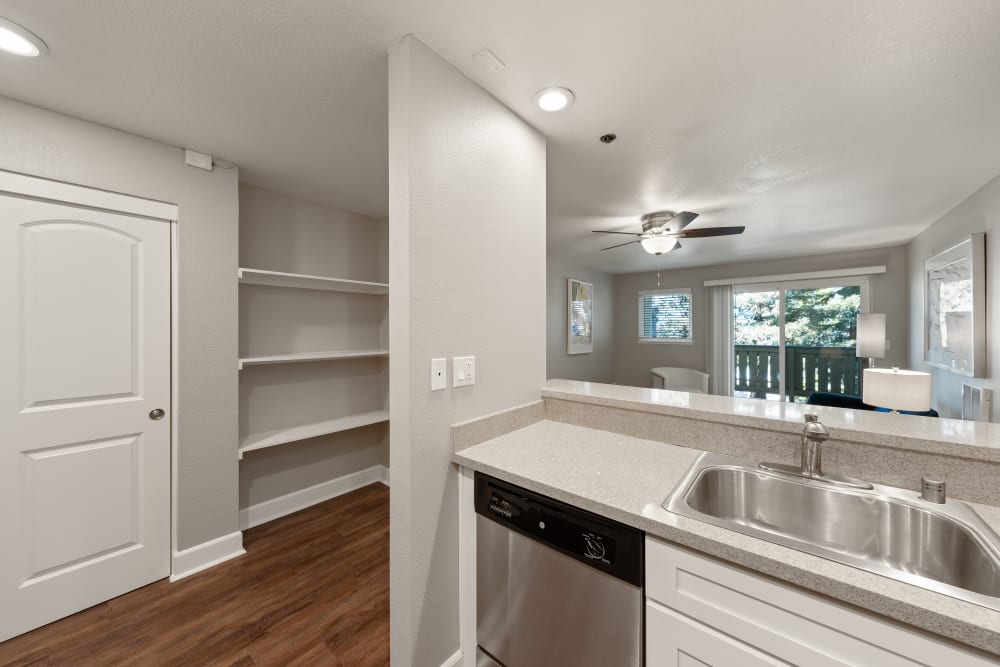 Kitchen with a dishwasher and oversized stainless-steel sink opening onto a hallway with built-in shelving at Summerhill Terrace Apartments in San Leandro, California