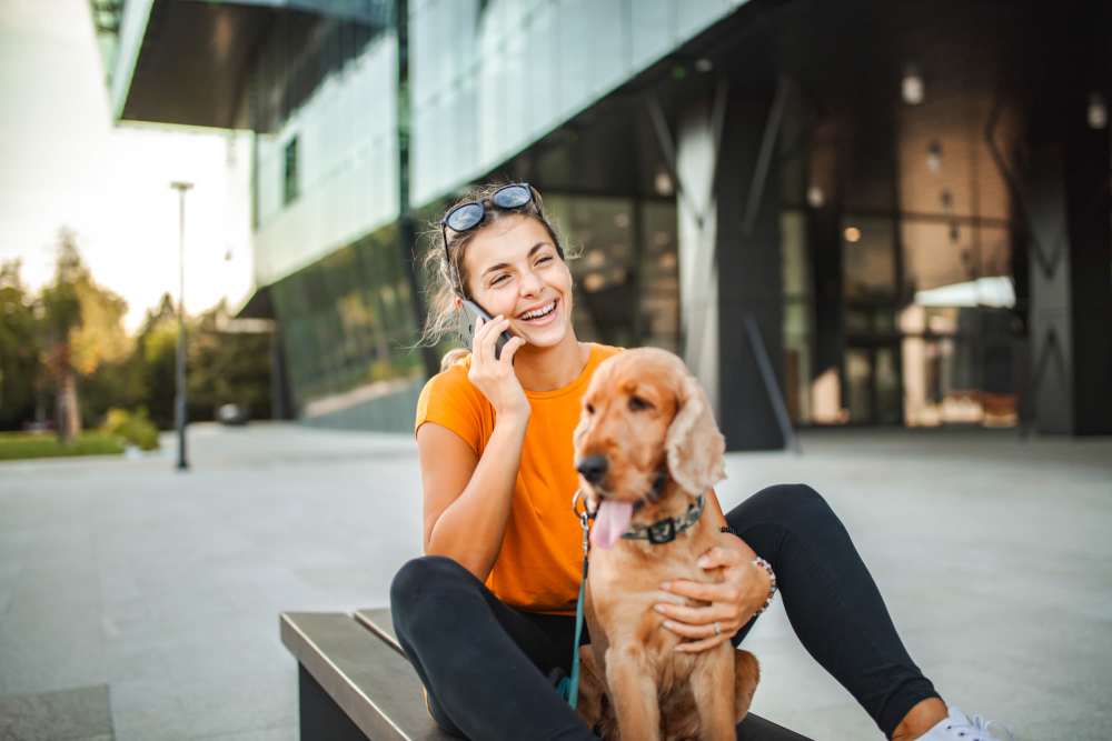 Woman sitting with her puppy while talking on her cell phone at Art Avenue Apartment Homes in Orlando, Florida