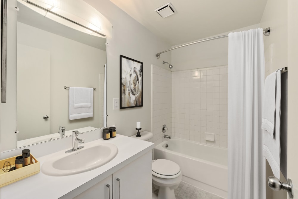 Model bathroom with white cabinetry, a large mirror, and tiled tub/shower at Farmington Oaks Apartments in Farmington, Michigan