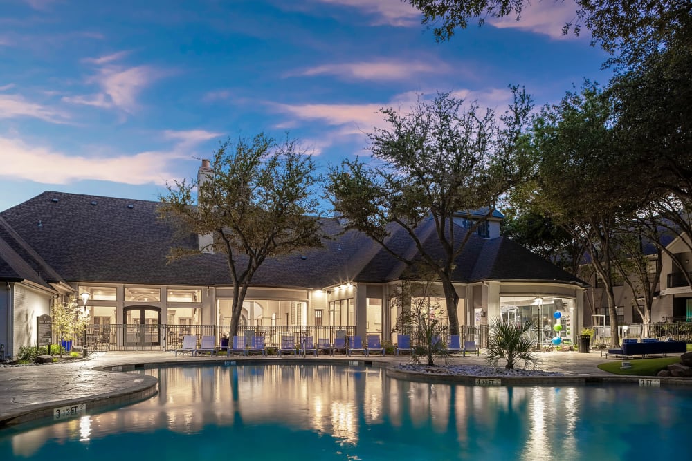 Pool deck area with tables and chairs covered by lush trees at Marquis at Waterview in Richardson, Texas