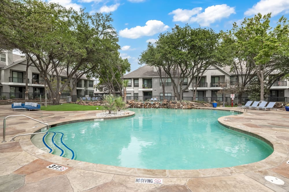 Pool deck area with tables and chairs covered by lush trees at Marquis at Waterview in Richardson, Texas