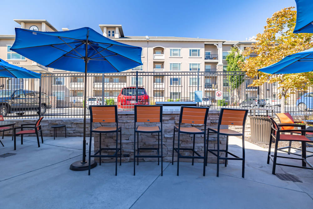 Outdoor seating area by swimming pool features high top tables and sun umbrellas at Meadowbrook Station Apartments in Salt Lake City, Utah