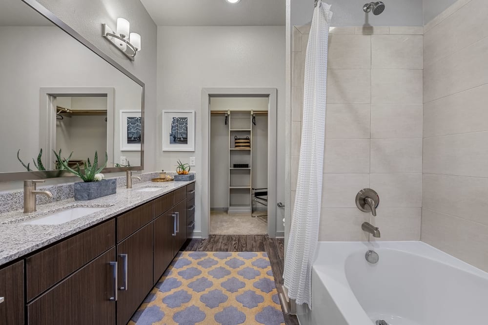 Large bathroom with double sinks, dark cabinets and walkway to large walk-in closet at Marq Uptown in Austin, Texas