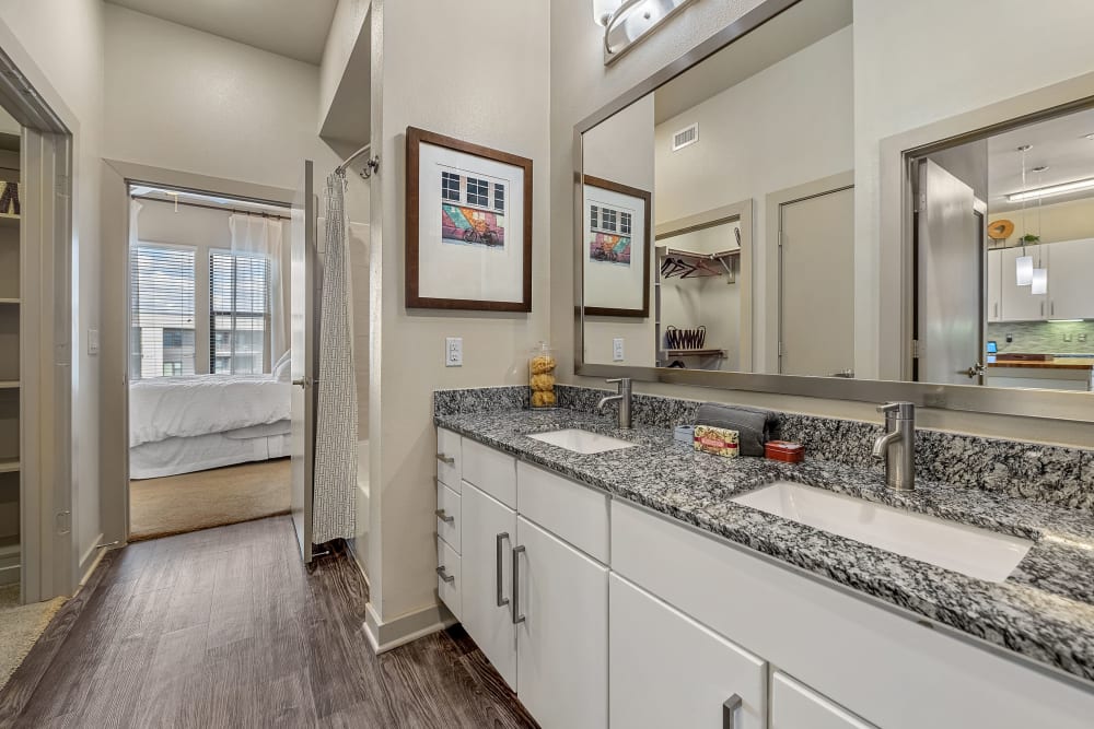 Large bathroom with double sinks, white cabinets and walkway to large walk-in closet at Marq Uptown in Austin, Texas