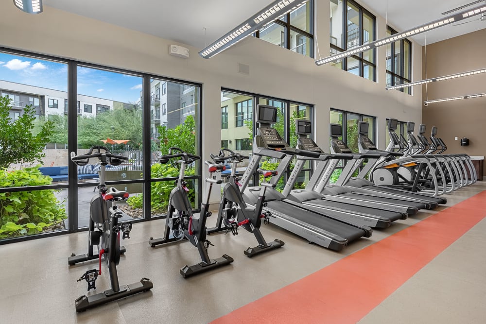 Multiple elliptical and treadmills lined up facing windows with view of pool deck at Marq Uptown in Austin, Texas