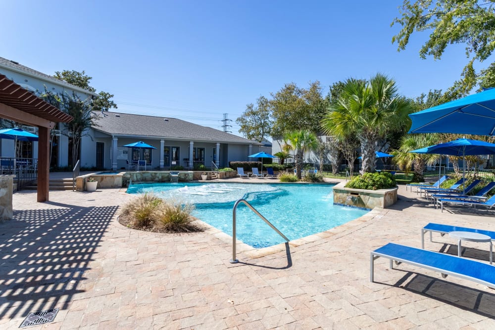 Community pool with lounge chairs and sunshades at Signature Point Apartments in League City, Texas