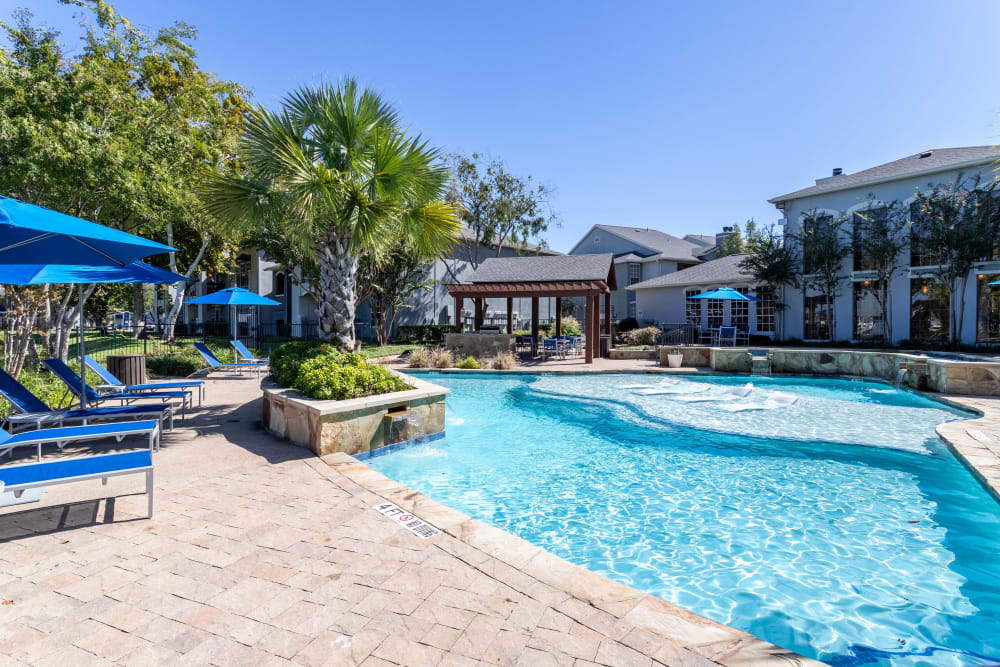 Poolside lounge chairs and tables with umbrellas at Signature Point Apartments in League City, Texas