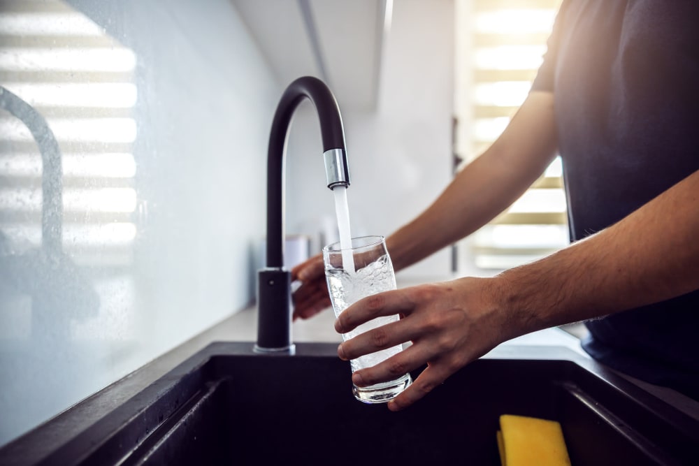 Resident filling his water glass from the gooseneck kitchen faucet over the large-basin sink in his apartment home at Las Terrazas in Colton, California